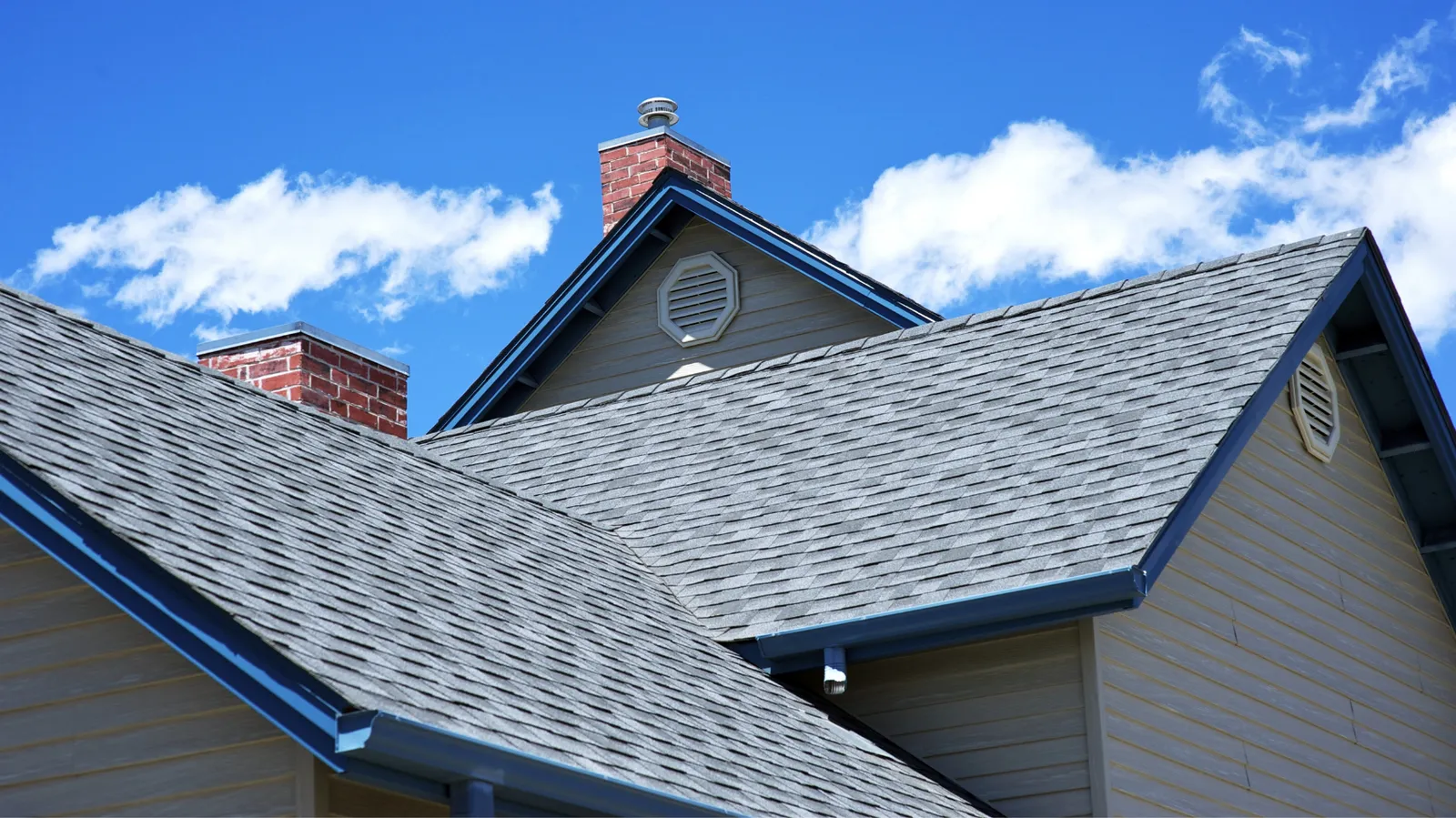 Bright blue sky behind gray shingle rooflines with brick chimneys