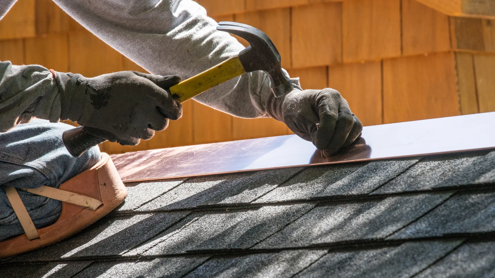 Metal flashing hammered along a shingle roof edge by a roofer