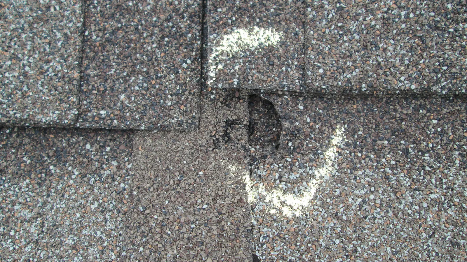 Chalk circle marking a hail impact and granule loss on shingles